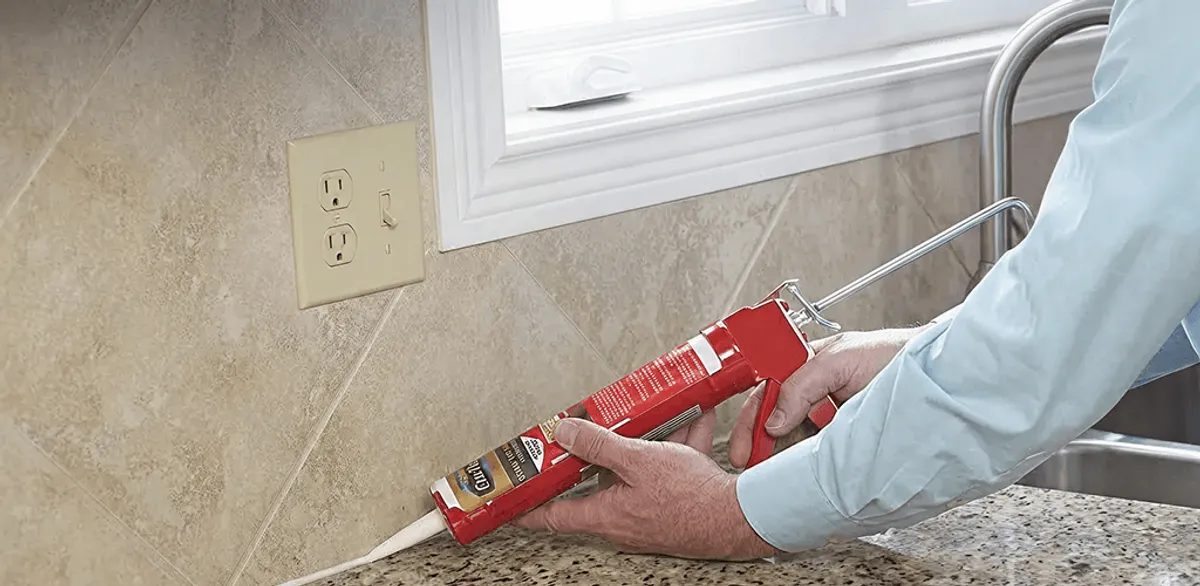 Handyman applying caulk along a kitchen backsplash and countertop seam in Tulsa, OK