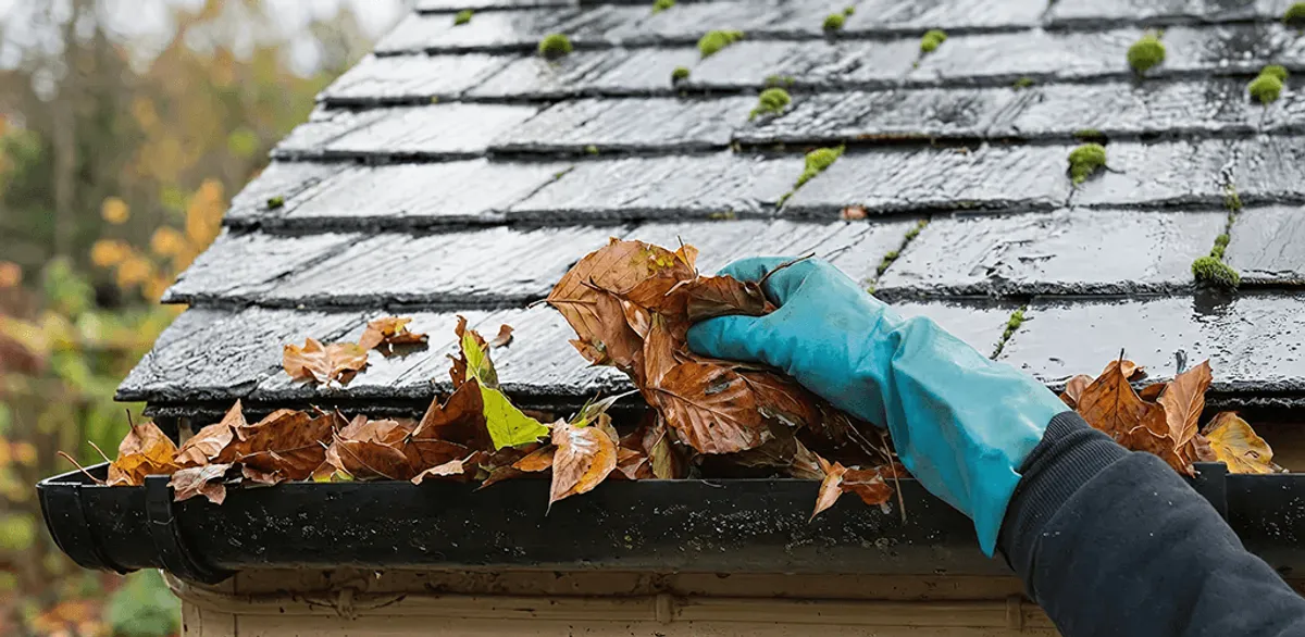 Gutter cleaning technician clearing wet leaves from roof gutters in Tulsa, OK