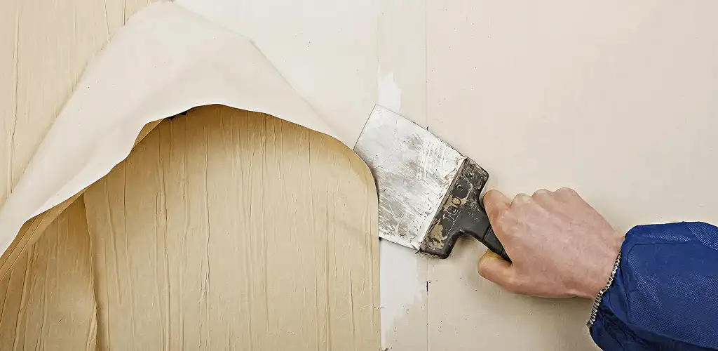 Handyman removing wallpaper with a scraper for wall preparation in Tulsa, OK