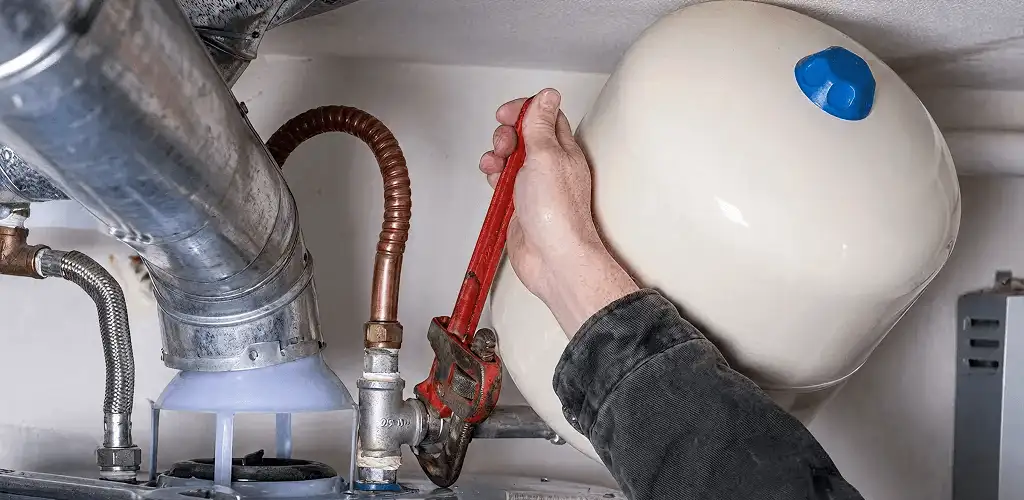 Water heater repair technician tightening plumbing connections near a tank unit in Tulsa, OK